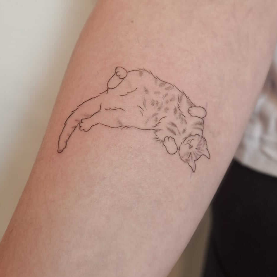 Tattoo einer liegenden Katze, die entspannt auf dem Unterarm dargestellt ist.