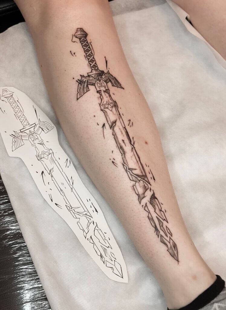 Tattoo eines Schwertes mit einem detaillierten Design und Bruchlinien auf dem Unterarm, neben der Schablone des gleichen Designs.