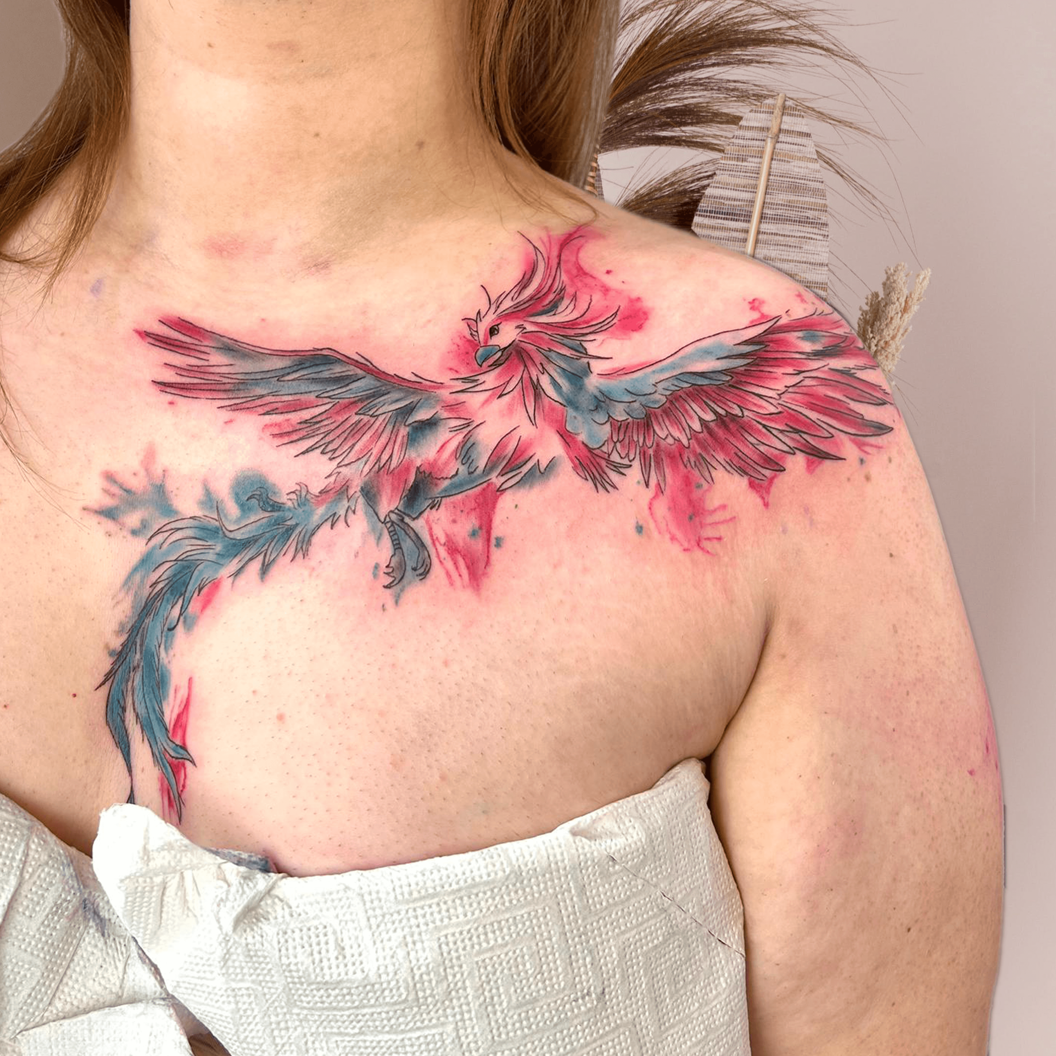 Tattoo eines Phönix, der in kräftigen Aquarellfarben auf der Schulter und dem Oberkörper dargestellt ist.