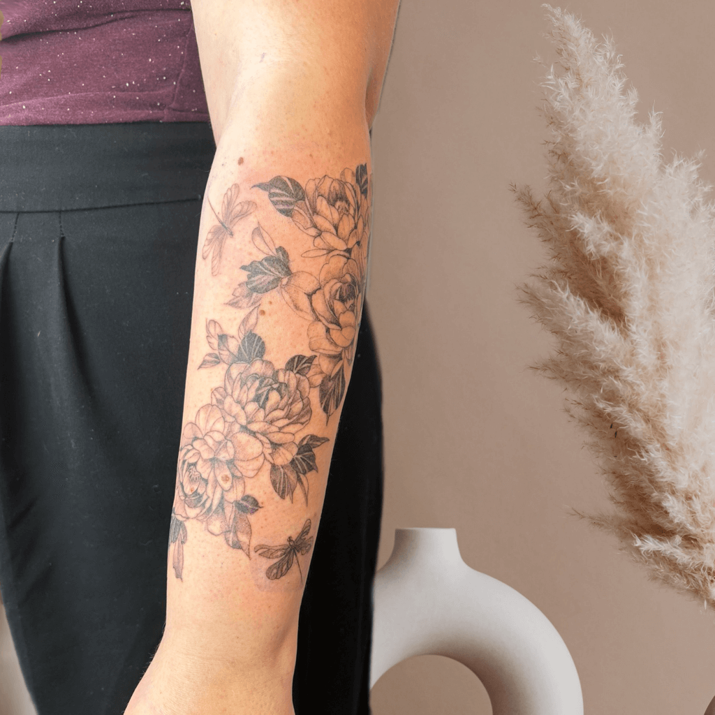 Tattoo einer floralen Komposition mit verschiedenen Blumen und Schmetterlingen, die auf dem Unterarm platziert sind.