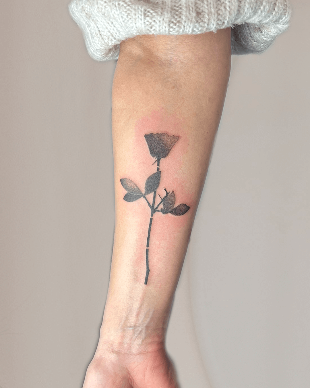 Minimalistisches Rosentattoo am Unterarm – schwarze Rose mit Blättern und filigranem Stiel in schlichter, moderner Gestaltung, depreche mode